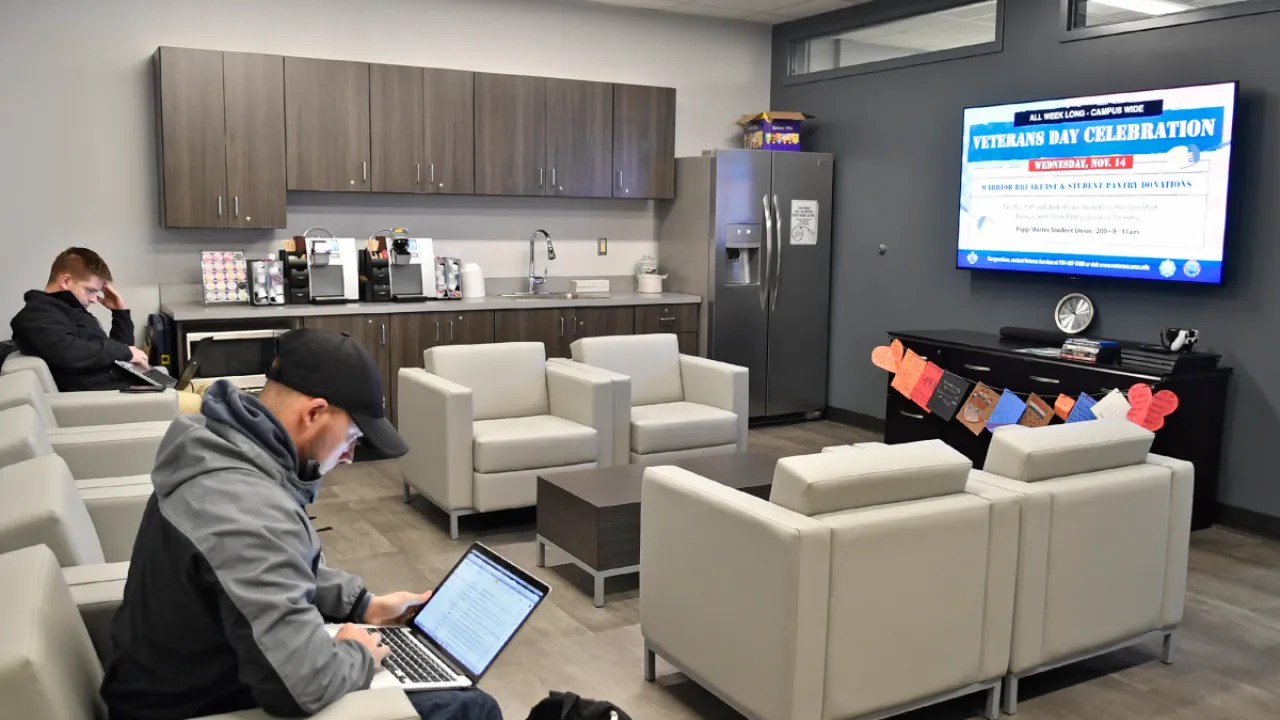 Two veteran students reading in the Veterans Lounge with soft chairs, kitchenette, and large tv